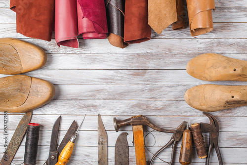 Set of cobbler tools and a lot of brightly colored leather in rolls on wooden background. Space for text. photo