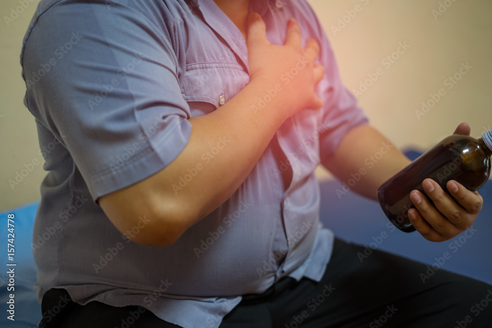A Fat man having chest pain, heart attack, He holding a bottle of medicine for himself. Health care concept. Close-up.