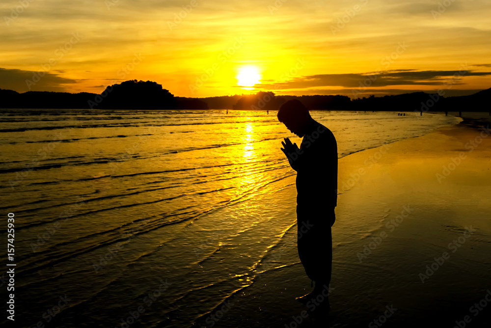  silhouette of young man praying on the beach with  golden sunset 