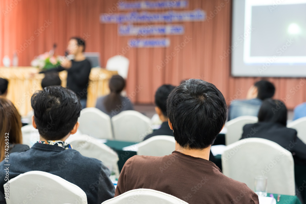 Blurred Speakers on the stage with Rear view of Audience in the conference hall or seminar meeting, business and education concept
