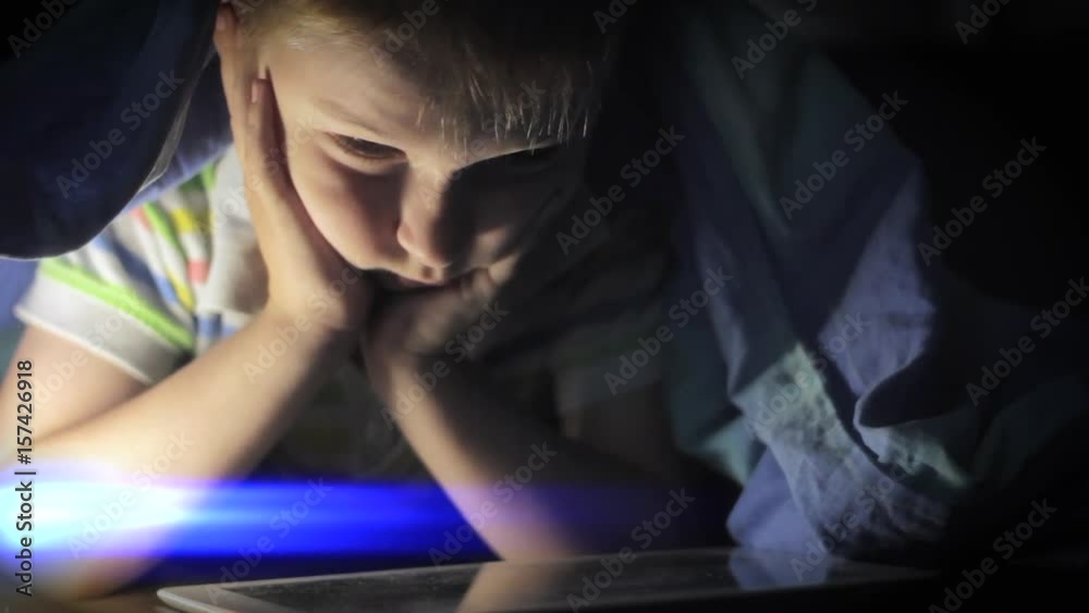 Boy lying under blanket and watching cartoon on touch pad Boy lying under blanket and watching cartoon on touch pad