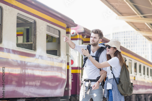 Young couple asian woman and caucasian man traveler are pointing and looking out with train station background. Travel in summer concept. Lover concept.