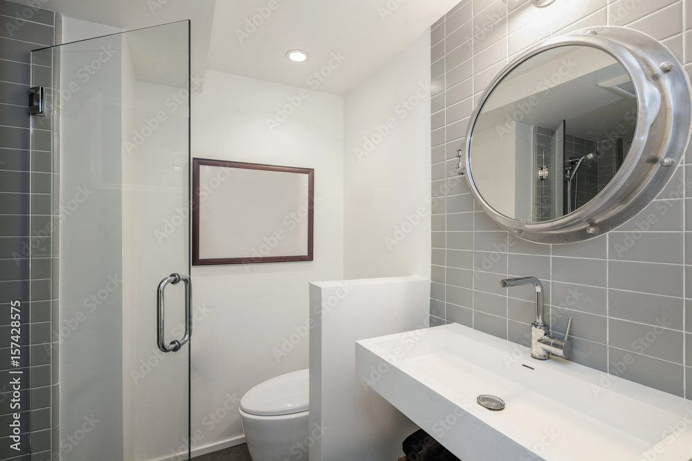 Clean modern bathroom with tiled wall and round mirror Clean modern bathroom with tiled wall and round mirror