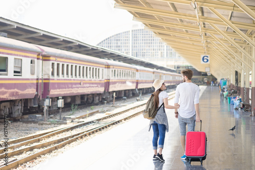 Young couple asian woman and caucasian man traveler are looking each together with train station background. Travel in summer concept. Lover concept.