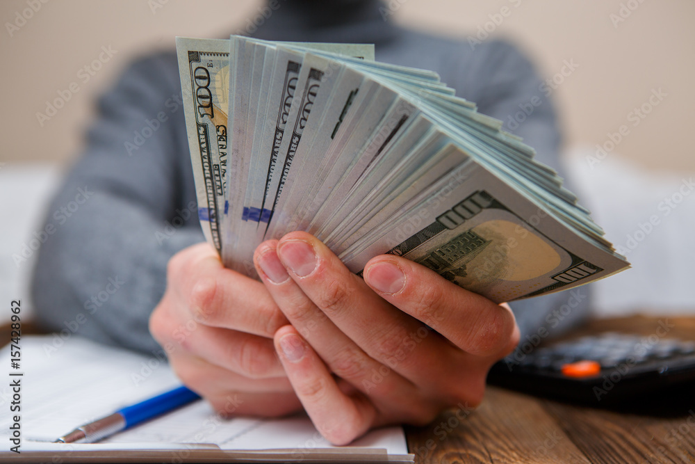 Caucasian hands counting dollar banknotes on dark wooden table Caucasian hands counting dollar banknotes on dark wooden table