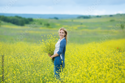 Genuine cute lady woman in meadow of yellow flowers sniffing flower bouquet. Attractive beautiful young girl enjoying the warm summer sun in a wide green and yellow meadow. Stylish dressed