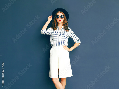 Fashion elegant lady woman wearing a black sunglasses, hat and white skirt posing over a gray background