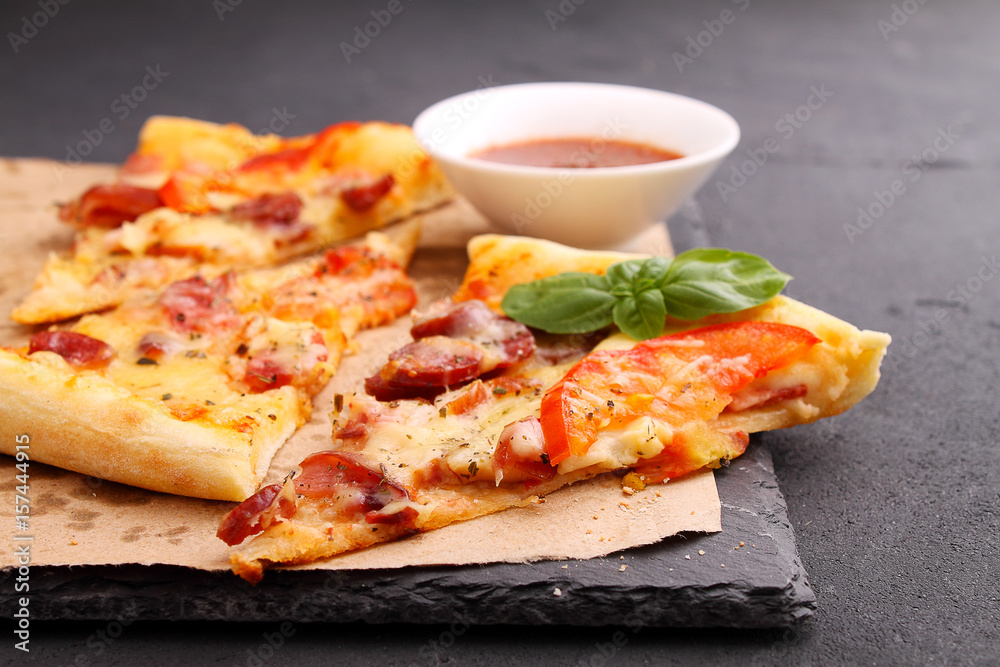 Pizza with sausage, ham, tomato and cheese, decorated with basil and cut into pieces on a parchment Pizza with sausage, ham, tomato and cheese, decorated with basil and cut into pieces on a parchment