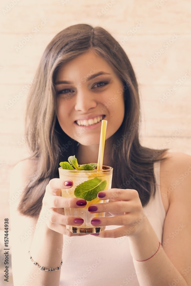 A glass of detox water with lemon, ice and fresh mint in the hands of a young girl. A glass of detox water with lemon, ice and fresh mint in the hands of a young girl.