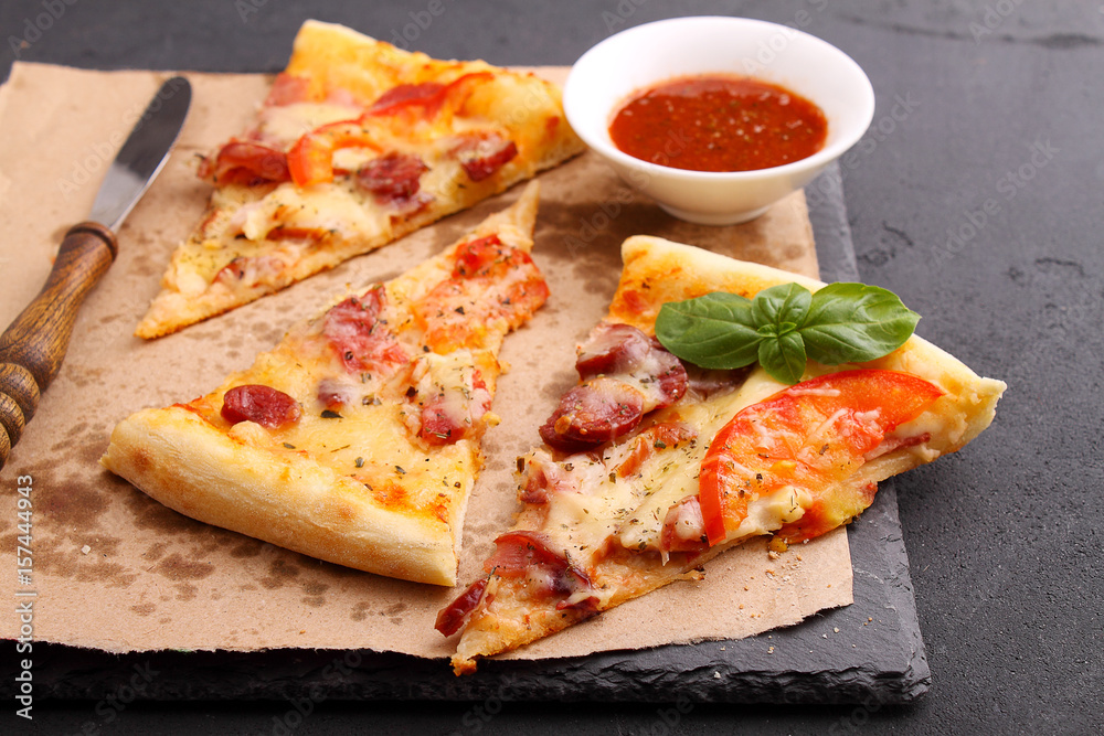 Pizza with sausage, ham, tomato and cheese, decorated with basil and cut into pieces on a parchment Pizza with sausage, ham, tomato and cheese, decorated with basil and cut into pieces on a parchment