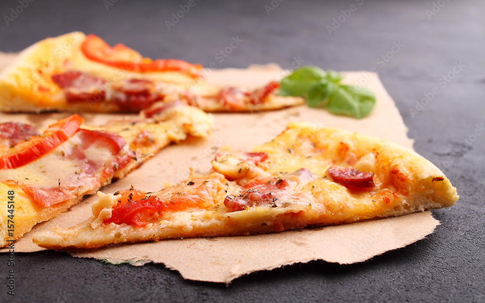 Pizza with sausage, ham, tomato and cheese, decorated with basil and cut into pieces on a parchment Pizza with sausage, ham, tomato and cheese, decorated with basil and cut into pieces on a parchment