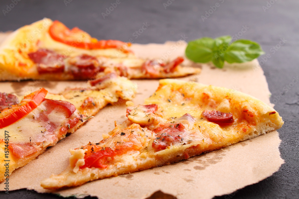 Pizza with sausage, ham, tomato and cheese, decorated with basil and cut into pieces on a parchment Pizza with sausage, ham, tomato and cheese, decorated with basil and cut into pieces on a parchment