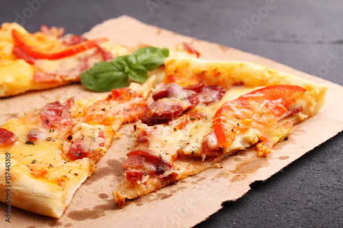 Pizza with sausage, ham, tomato and cheese, decorated with basil and cut into pieces on a parchment