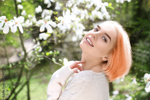 Young blonde girl near blooming magnolia tree on blurred background