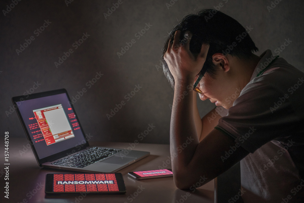 Young Asian male frustrated, confused and headache by WannaCry ransomware attack on desktop screen, notebook and smartphone, cyber attack internet security concept Young Asian male frustrated, confused and headache by WannaCry ransomware attack on desktop screen, notebook and smartphone, cyber attack internet security concept