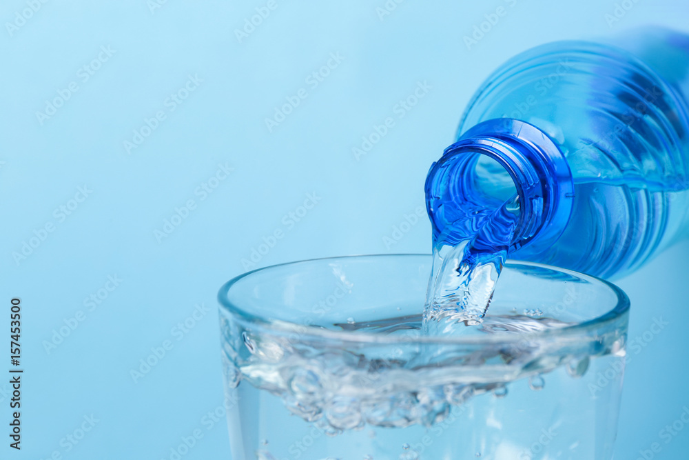 Water pouring from bottle into glass on color background Water pouring from bottle into glass on color background