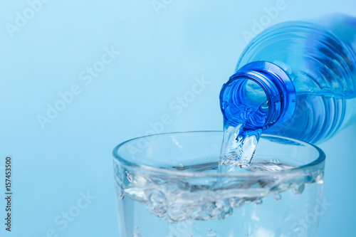 Water pouring from bottle into glass on color background