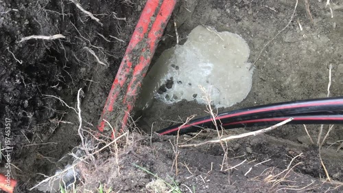 Electrical cable being buried in a large hole with other communication cables; camera pans up to wooden spool at end.  