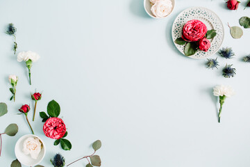 Flowers border frame made of red and beige roses, white carnation and eucalyptus branches on pale pastel blue background. Flat lay, top view. Floral texture background.