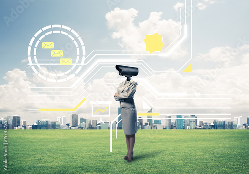 Camera headed woman standing on green grass against modern citys