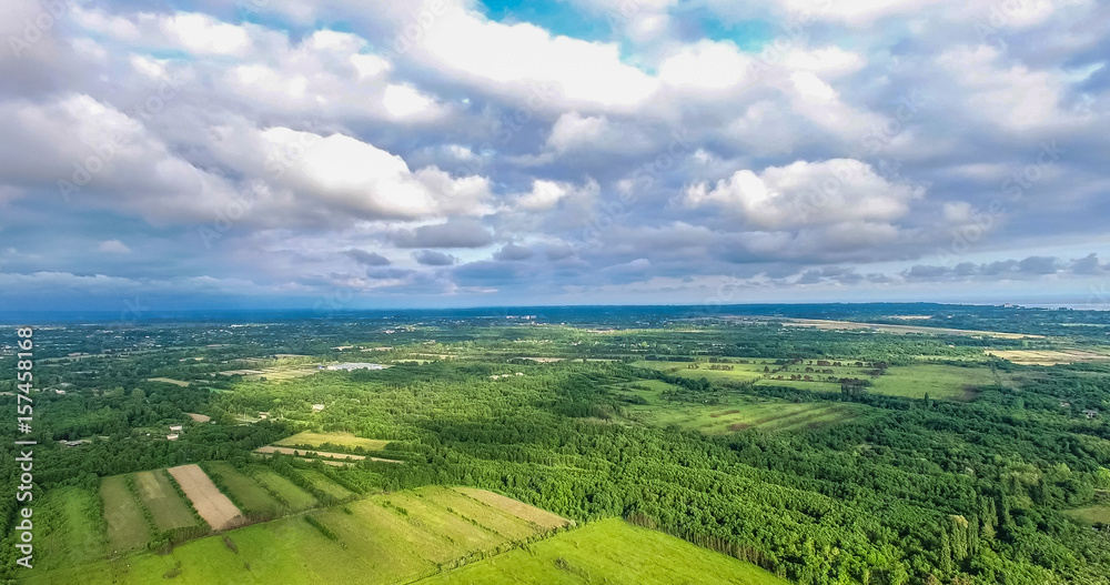 view from the quadrocopter to the fields and forests under the clouds