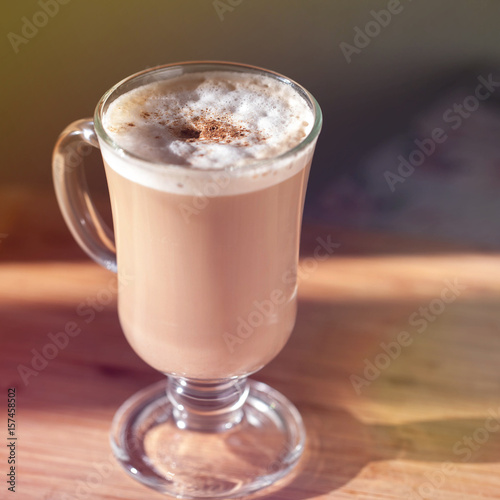Glass cup with cappuccino on the table. Smooth focus. Cinnamon. Sunlight, toned