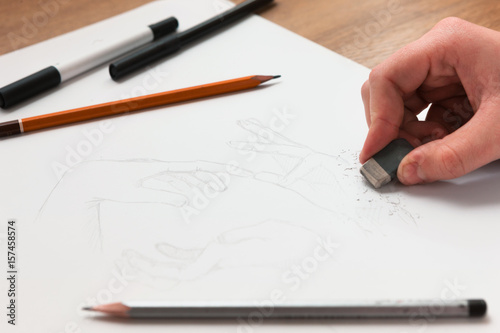 From above hand erasing lines on a sketch. Horizontal indoors shot. Drawing lessons, art school, young artist concept