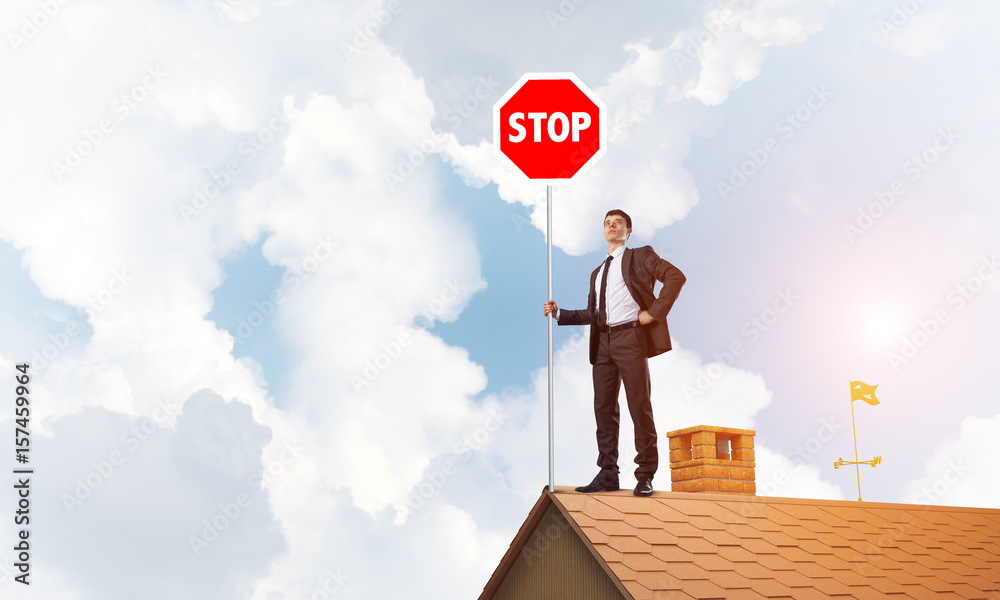 Caucasian businessman on brick house roof showing stop road sign. Mixed media