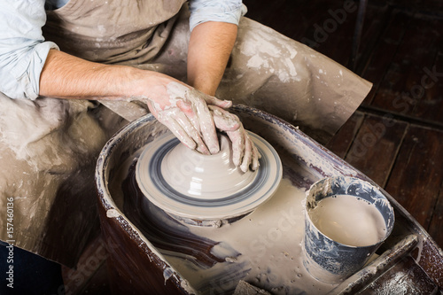 pottery  workshop  ceramics art concept - closeup on working potter s wheel with raw clay and man hands  a male sculpt a utensil with fingers  master in apron  top view