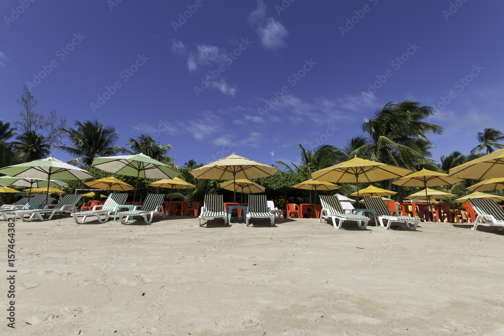 Colorful umbrella and beach chair on tropical beach with coconut trees and blue sky, vacation concept