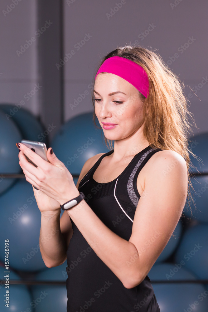 Fototapeta premium Young woman with fitness tracker and smartphone in gym