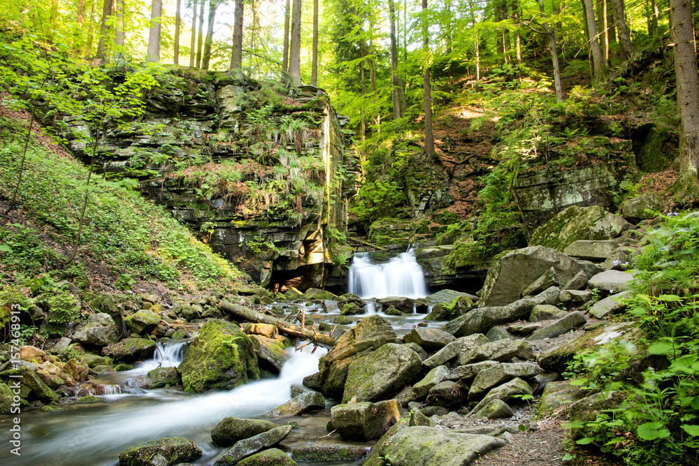 Fototapeta premium Wodospad w otoczeniu skał i drzew.