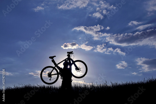 silhouette of a cyclist with a raised bike in the sun.