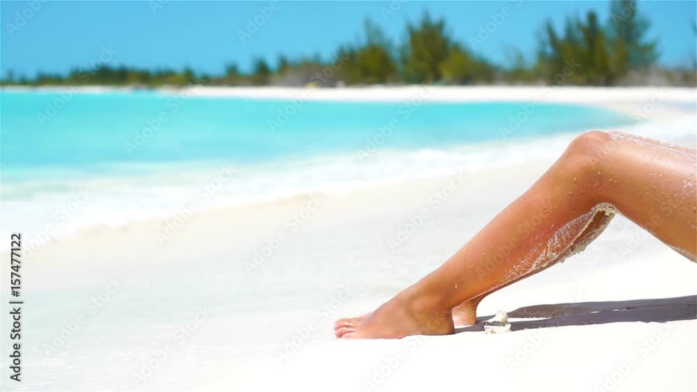 Female slim tanned legs on a white tropical beach. SLOW VIDEO