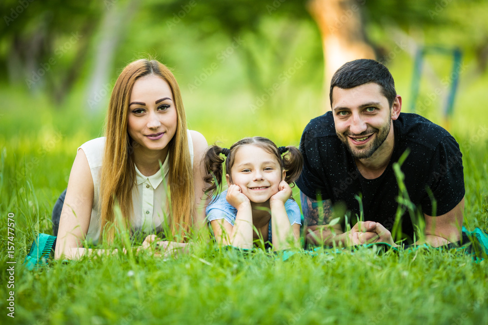 Portrait of a happy family of three lying in the lawn, having fun Portrait of a happy family of three lying in the lawn, having fun