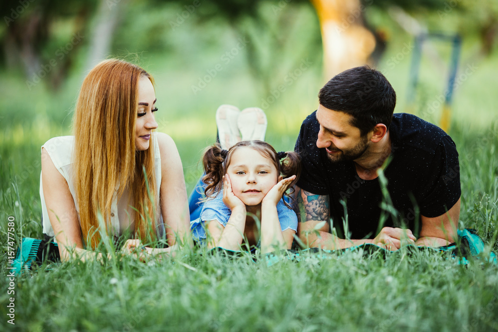 Happy family of three lying on grass. Concept of happy family relations and carefree leisure time Happy family of three lying on grass. Concept of happy family relations and carefree leisure time