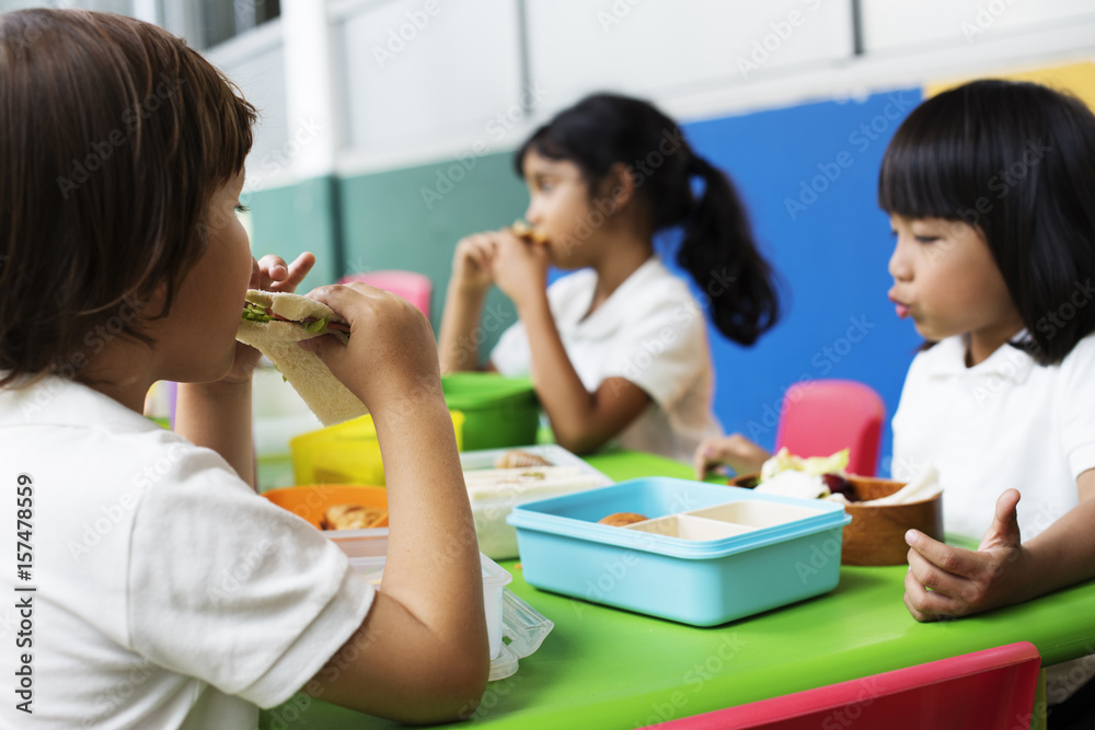 Group of Kindergarten Students Eating Food Lunch Break Together - obrazy, fototapety, plakaty 