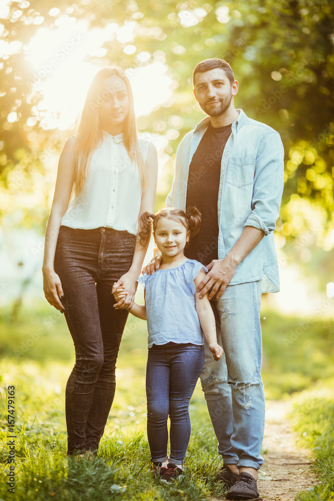 Fototapeta premium Happy mother, father and daughter in sunset in summer park