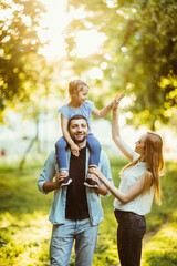 happy family Mom and Dad holding daughter on his back and have fun in the park.