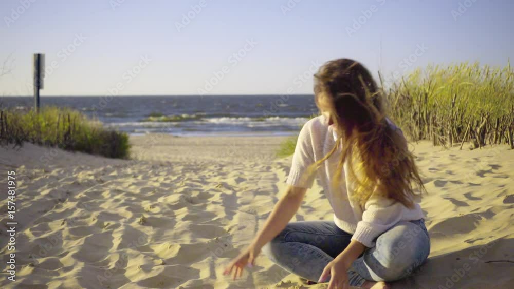 Beautiful girl playing with sand on beach. Young woman having fun sitting on sandy grassy dunes, relaxing on the sea coast. Vacation happiness and freedom concept 4K ProRes HQ codec Beautiful girl playing with sand on beach. Young woman having fun sitting on sandy grassy dunes, relaxing on the sea coast. Vacation happiness and freedom concept 4K ProRes HQ codec