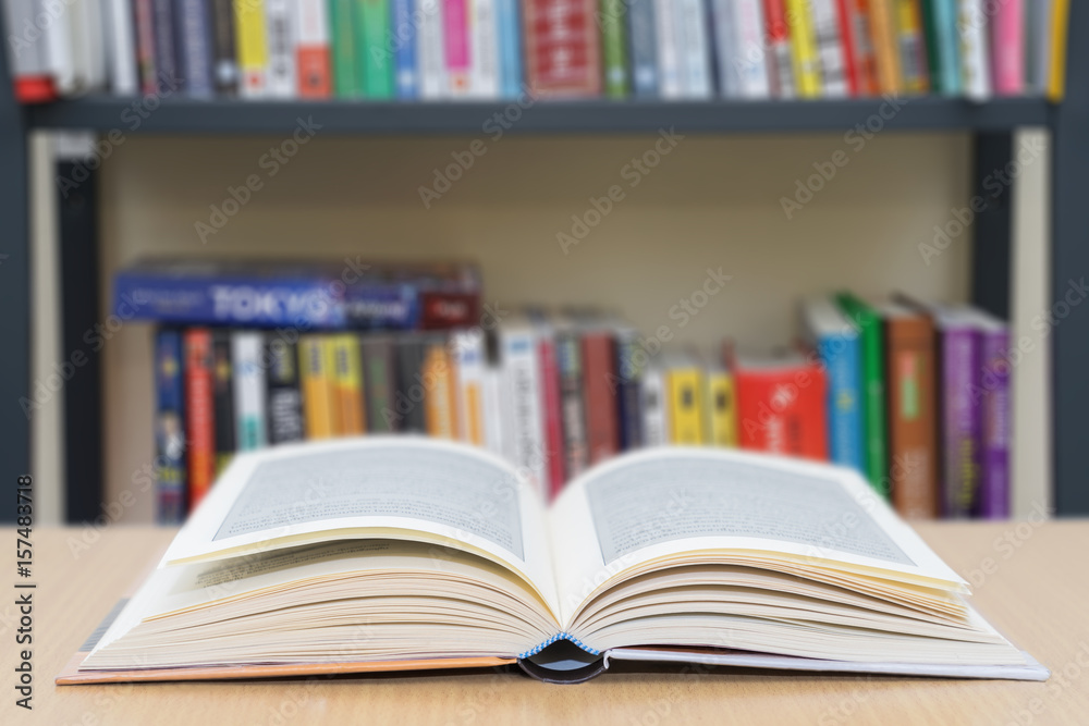 Open book on wood top with blured bookshelf background. Open book on wood top with blured bookshelf background.