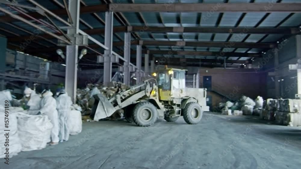PAN of small bulldozer driving in warehouse of garbage recycling ...