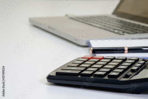 close up side view numeric keypad of calculator and blurred ball pen, laptop on white desk for business; financial; investor; accounting concept.