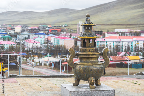 Mongolian metal religious statue on granite pedestal with city landscape on background