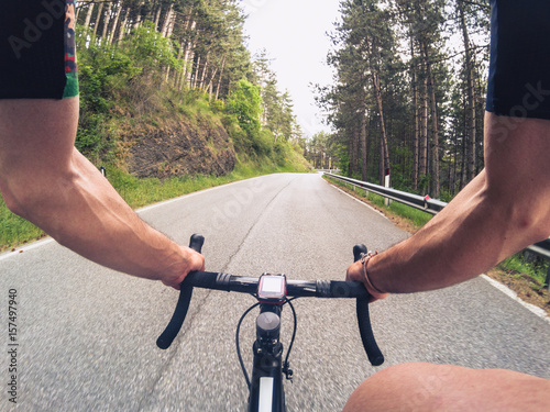 Fotografie Young adult man climbing a mountain road with a racing bicycle on a spring afternoon