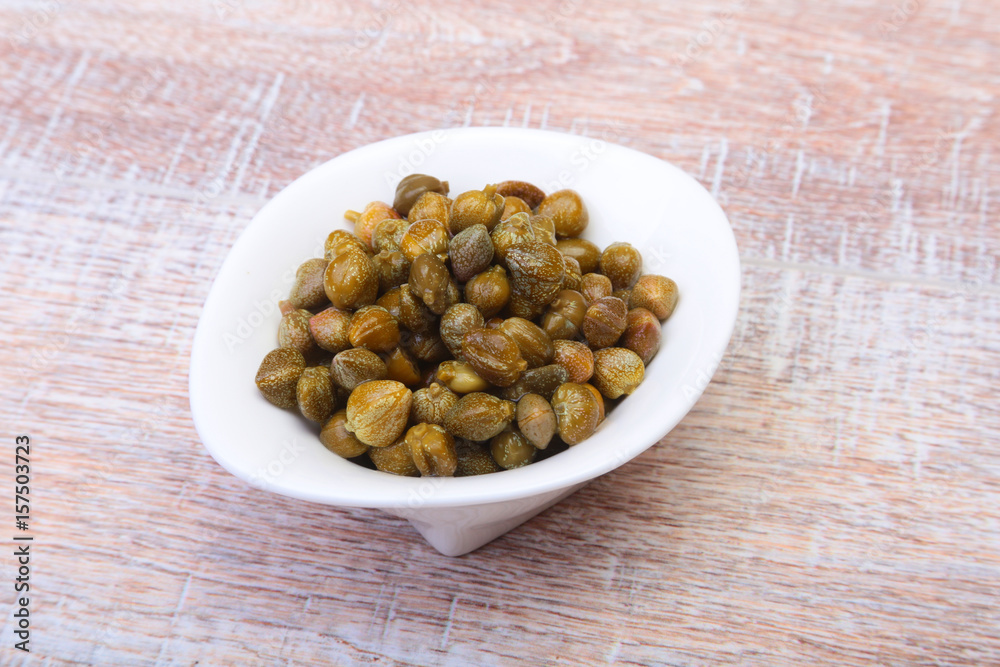 bowl with fresh capers on wooden table