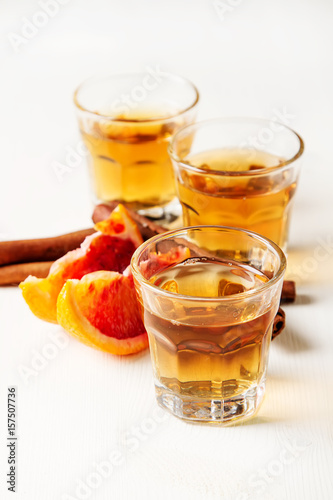 Golden tequila with red orange and cinnamon. Light white background. Selective focus