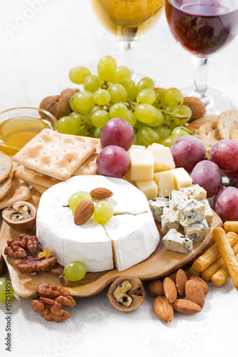 camembert, grapes, wine and snacks on a white table, vertical