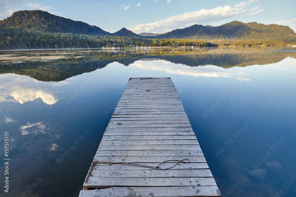 Fototapeta premium Pier on the lake on the background of sunset in a clear summer day. Warm summer evening on the dock. Fabulous views of the lake and the bridge in the sunlight
