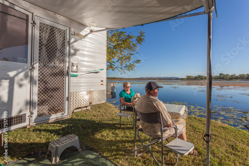 Retired couple sitting outside of caravan with small dog enjoying a wine next to the Lilly filled Lake Kununurra photo